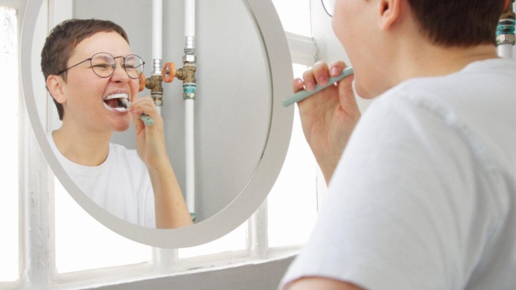Person brushing their teeth while looking in a mirror.