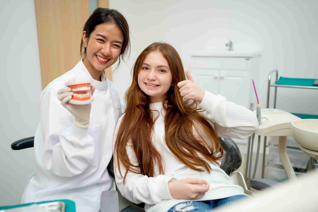 Smiling dentist with young patient giving thumbs up while holding a dental model.