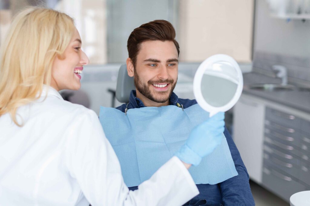 Dentist showing a hand mirror while patient smiles.
